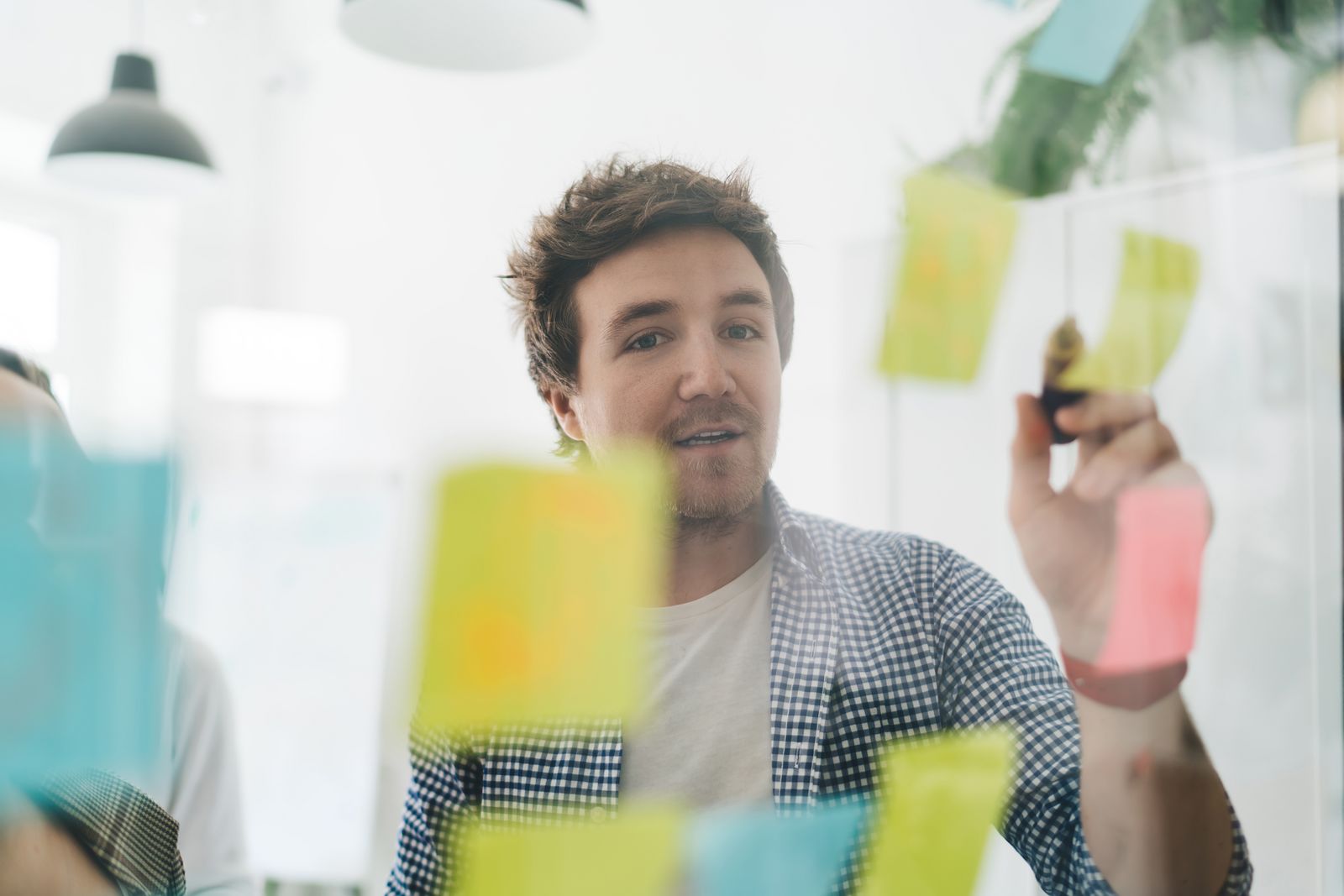 Design mit einem Stift in der Hand schreibt auf einer Glasscheibe mit PostIts